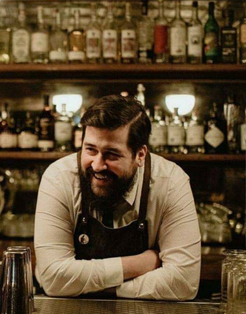Chris Mallon behind the bar mid-shift, smiling while bartending- an authentic thankful moment from his 26-year journey in hospitality