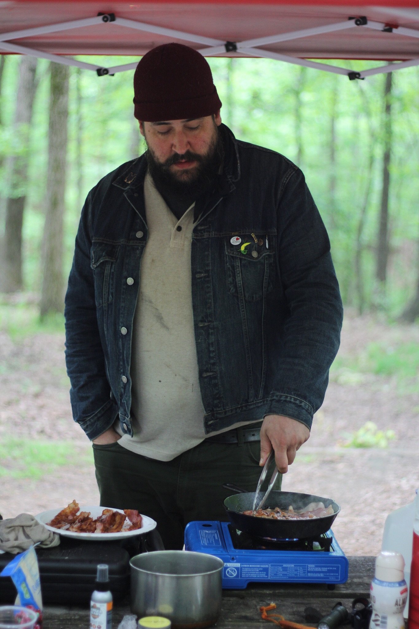Chris Mallon cooking outdoors in fall, standing over a camp stove in a rustic setting
